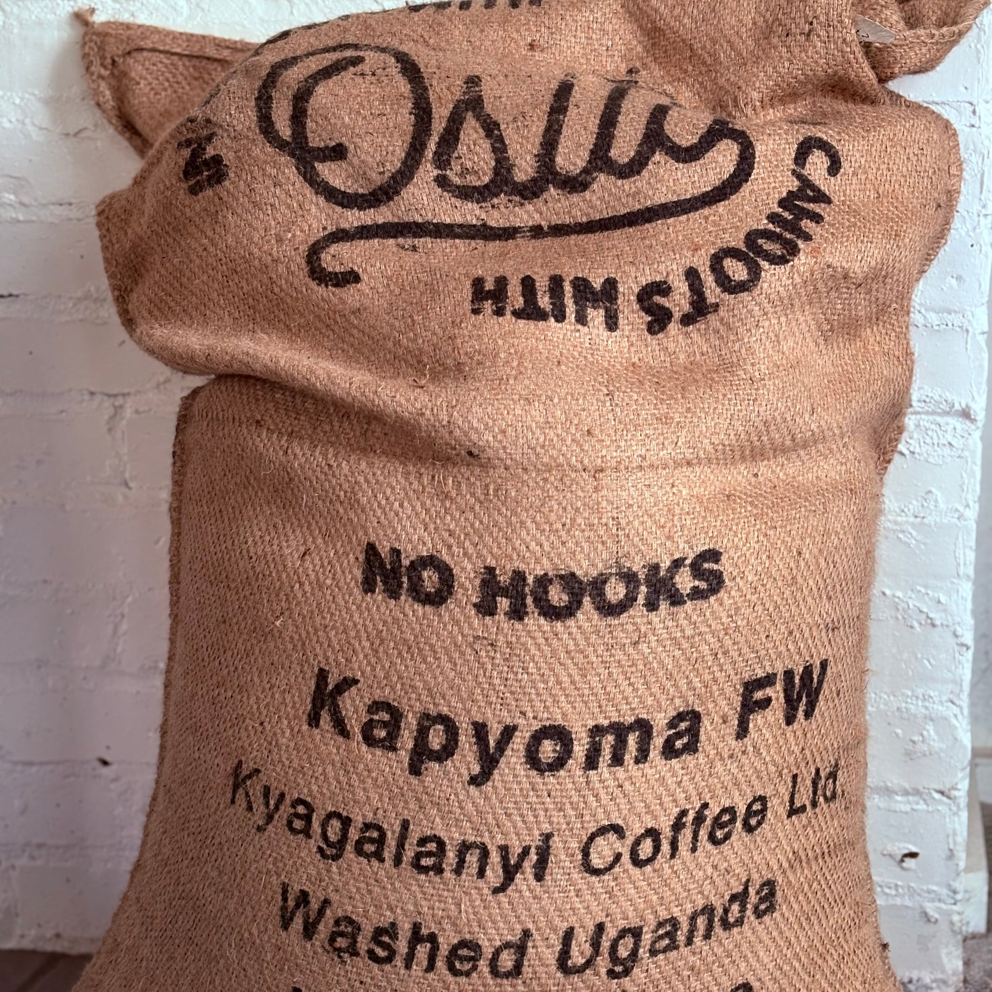 Brown burlap coffee sack with black text against a white brick wall.