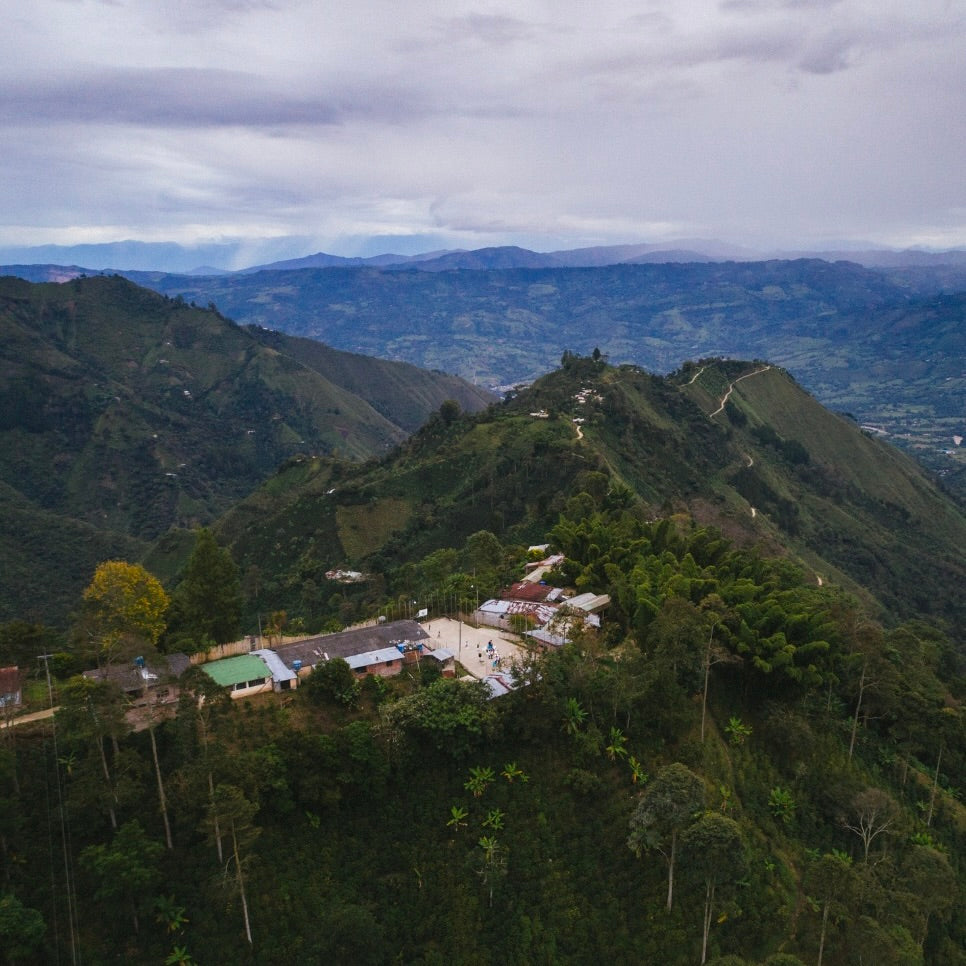 Village nestled in a Colombian valley surrounded by green mountains under a cloudy sky.